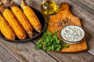 Koyu ahşap bir arka plan üzerinde ahşap bir tahta üzerinde otlar ile koçan üzerinde ızgara mısır.