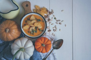 Sıcak sonbahar balkabağı çorbasıyla ahşap kırsal masa manzaralı, kasede susam tohumları süslenmiş. Cadılar Bayramı menüsü için rahat bir yaşam tarzı.