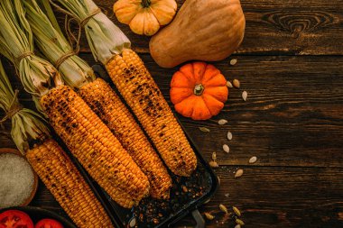 Koyu ahşap bir arka plan üzerinde ahşap bir tahta üzerinde otlar ile koçan üzerinde ızgara mısır.