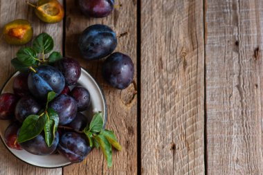 Yeşil yapraklı rustik masada eski bir kapta taze erik yığını. Tonlu görüntü. Yumuşak odak. Kopyalama alanı.