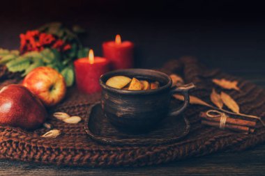 Sonbahar yaprakları, sıcak bir fincan çay, örme battaniye, kırmızı meyveler, ahşap masa arka plan üzerinde mumlar. Mevsimlik, sonbahar sıcak içeceği. Sonbahar rahatlatıcı ve natürmort kavramı. Tonlu görüntü. Seçici odaklama.