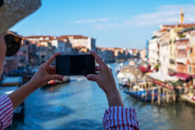 Venedik, İtalya 'daki ünlü Rialto Köprüsü' nden panoramik manzara. Açık hava yaz yaşam tarzı. Akıllı telefonlu genç bir kadın seyahat fotoğrafı çekiyor..