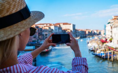 Venedik, İtalya 'daki ünlü Rialto Köprüsü' nden panoramik manzara. Açık hava yaz yaşam tarzı. Akıllı telefonlu genç bir kadın seyahat fotoğrafı çekiyor..