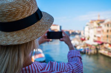 Venedik, İtalya 'daki ünlü Rialto Köprüsü' nden panoramik manzara. Açık hava yaz yaşam tarzı. Akıllı telefonlu genç bir kadın seyahat fotoğrafı çekiyor..