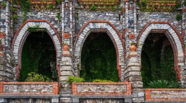 Kemerli ve yeşil yapraklı eski tuğla duvar. Yıpranmış duvar yüzeyi. Grunge duvar arka planı. Kalitesiz bina cephesi. Soyut. Boşluğu kopyala.