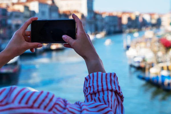 Technology, travel, tourism, hike and people concept. Young woman taking photos with her smartphone on famous Rialto Bridge of Grande Canal in Venice, Italy.