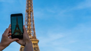 Paris 'teki Eyfel Kulesi. Güneş ışığı ve mavi gökyüzü altında. Dünyaca ünlü popüler turist mekanı. Paris 'te turist Fransa' yı geziyor, kadın cep telefonuyla fotoğraf çekiyor..