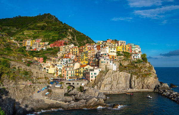 Manarola typical Italian village in National park Cinque Terre, colorful multi colored buildings houses on rock cliff, fishing boats on water, blue sky background, Liguria, Italy