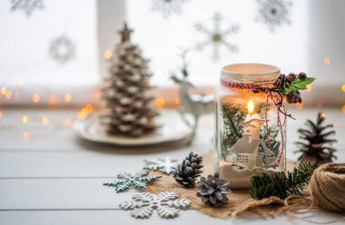 Klasik Noel geçmişi. Kömür dalı, çam kozalağı ve kış penceresine karşı yılbaşı süslemeleri olan kır masasının üzerinde Noel mumu feneri. Günaydın, sihirli ışık..