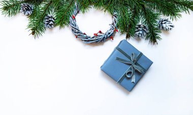 Noel kompozisyonu. Çelenkler, kırmızı böğürtlenler, köknar dalları, mavi hediye kutusu ve pastel gri arka planda çam kozalakları. Noel, kış, yeni yıl konsepti. Düz konum, üst görünüm, kopyalama alanı.