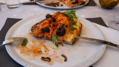 Tabakta pişmiş calzone var. Kapalı pizza türü, arka planda fesleğen dallarıyla süslenmiş..