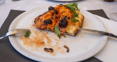 Tabakta pişmiş calzone var. Kapalı pizza türü, arka planda fesleğen dallarıyla süslenmiş..