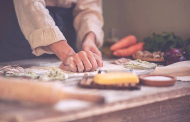 Koyu ahşap masa manzarasında makarna malzemeli taze ev yapımı makarna. Dişi, eski ahşap masanın üzerinde un ve yumurta ile ev yapımı makarna yapıyor..