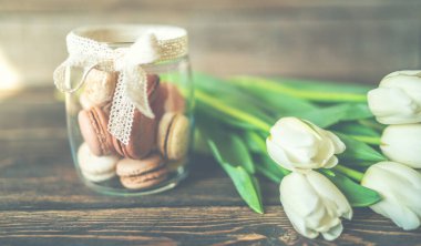 Bahar çiçekleri. Kahverengi ahşap masada beyaz laleler ve badem kurabiyeleri. Anneler Günü ve Sevgililer Günü geçmişi. Kırsal tarzda. Metnin için boşluk kopyala.