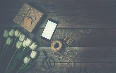 İndirim gününde ahşap arka planda akıllı telefonlu, hediyeli ve çiçekli maket imajı. Pazarlama ve yaratıcı iş tasarımı. Reklam için düzenleme.
