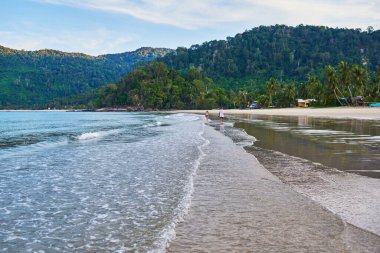 Güzel sahil. Etrafı avuçlarla çevrili güzel tropikal plajların doğal manzarası. Tatil, tatil, yaşam tarzı konsepti. Çift sahilde güzel bir yürüyüş yapıyor. Tioman Adası, Malezya.