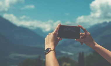 İsviçre Alplerinin resmini çekmek için akıllı telefon kamerası kullanan genç bir kadın. Yaz tatili sırasında cep telefonuyla fotoğraf çeken kadın gezgin blogcu.