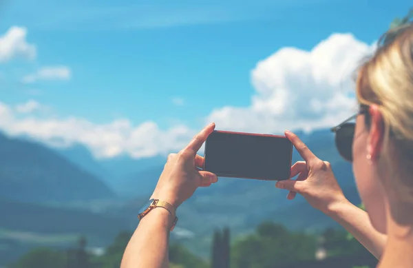スイスアルプスを撮影するためにスマートフォンのカメラを使用して若い女性のバックビュー 女性旅行ブロガーは夏の旅行休暇中に携帯電話で写真を撮る — ストック写真