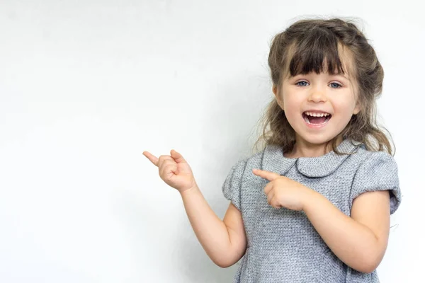 Portretul unui copil fericit care pozează și zâmbește cu o expresie nebună, arătând spre spațiul liber pentru publicitate. Copiați spațiul — Fotografie, imagine de stoc