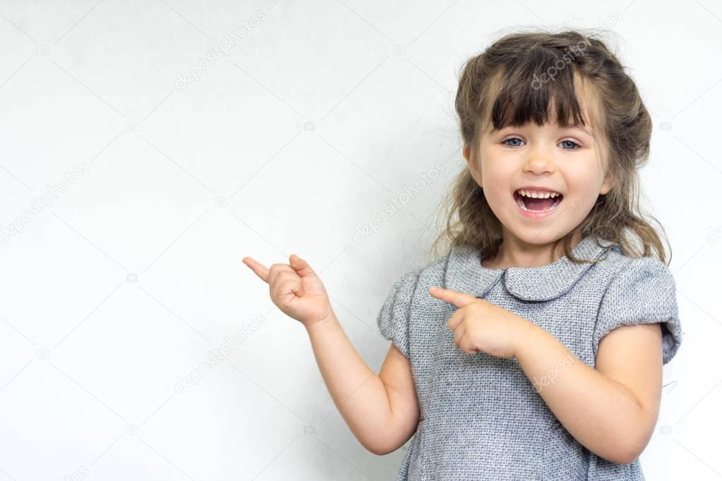 Portrait of joyful child posing and smiling with crazy expression, pointing at free space for advertisement. Copy space