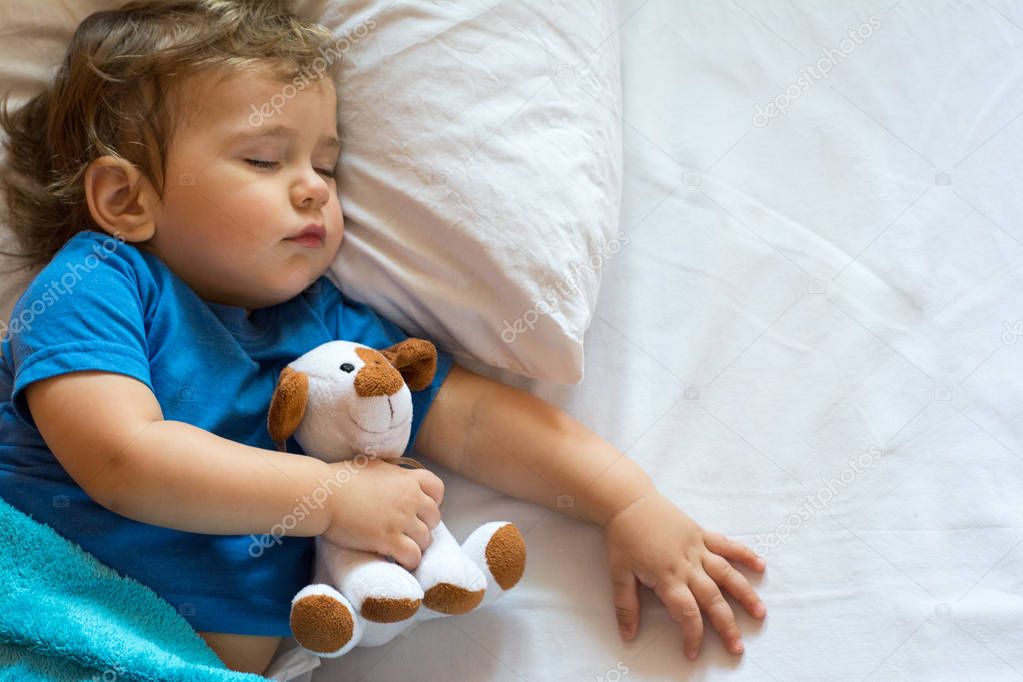 Cute toddler sleeping on the bed at home with toy. Free space