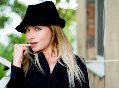 Closeup görünümü dikey olan bir çekici şehvetli seksi kadın sarışın saç ve parlak makyaj dudaklar kapalı yakınındaki parmak ile siyah yün şapkalı, kameraya, seyir Zemin, yatay resim bulanık