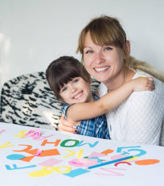 Gülümseyen genç şirin anne ve kızı bir parlak büyük beyaz odada yazmak öğrenme portresi. Yetişkin kadın çocuk alfabeyi öğretir..