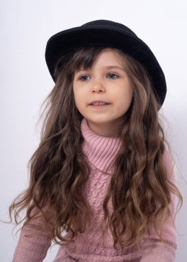 5-6 yaşlarında uzun kıvırcık saçlı ve siyah şapkalı beyaz arka planda poz veren bir çocuk. Mutlu yüz ifadesi. İzole edilmiş Ad