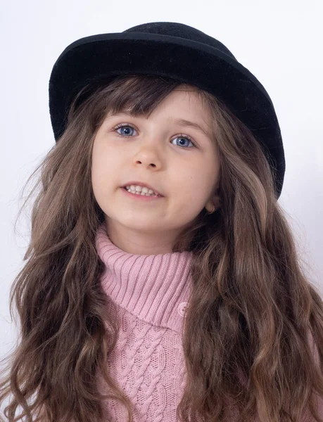長い巻き毛と白い背景にポーズ黒の帽子を持つ5 6歳の子供 幸せな表情だ孤立広告 — ストック写真