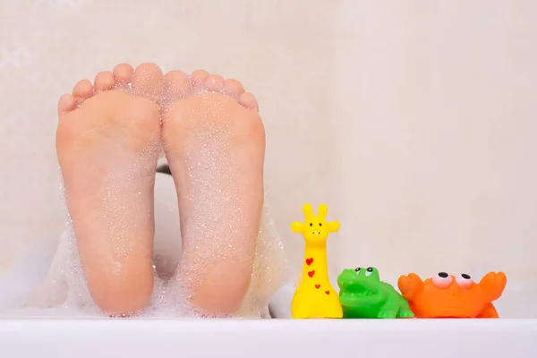 可爱的小女孩在一个白色的浴室里玩泡沫和五颜六色的橡胶玩具洗澡 — 图库照片