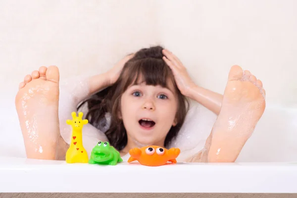 Güzel küçük kız köpüklü bir küvette banyo yapıyor. Duşta saçını şampuanla yıkayan tatlı bir çocuk..