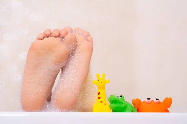 Çocuklar köpük banyosu yapıyor. Çocuk küvette banyo yapıyor. Küçük kız suyla oynuyor. Köpük banyosunda plastik oyuncaklar