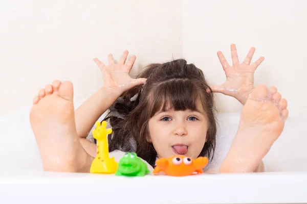 Çocuklar köpük banyosu yapıyor. Çocuk küvette banyo yapıyor. Küçük kız suyla oynuyor. Köpük banyosunda plastik ördek.