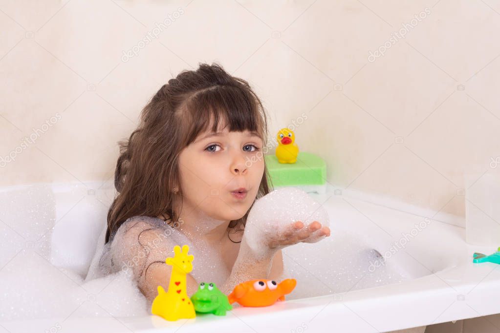 Kids taking bubble bath. Child bathing in bathtub. Little girl playing with water. Rubber toys in foam bath.