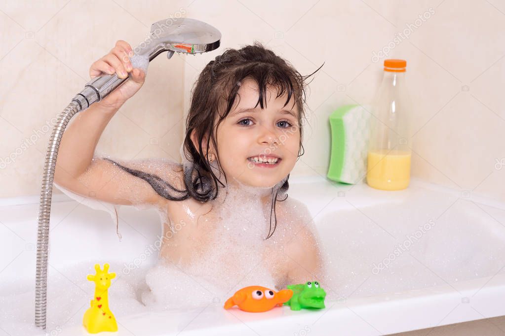 Beautiful toddler girl taking a bath in a bathtub with bubbles. Cute kid washing his hair with shampoo in the shower.