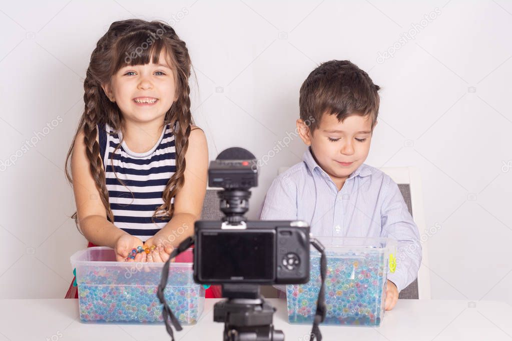 Girl and boy playing and talking on camera at home, they make video blog. Little kids reviewing toys on camera while recording a video blog