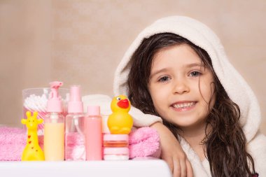 Bebek aksesuarları ve oyuncaklar banyoya karşı. Sıvı sabun paketi, şampuan şişesi, sünger, plastik oyuncak ve beyaz arka planda havlu.. 