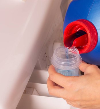 Çamaşır makinesi için bir şişe deterjan. Çamaşır günü. Kadın çamaşır makinesine fosfatsız çamaşır jeli döküyor.. 