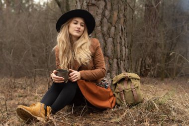 Sırt çantalı, kamp çadırının yanında oturan güzel, gülümseyen kız, şenlik ateşi. Seyahat tatili. Mutlu kadın haftasonu doğada sırt çantasıyla geziyor.. 