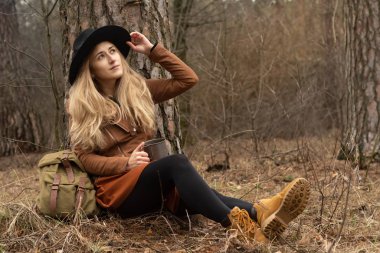 Sırt çantalı, kamp çadırının yanında oturan güzel, gülümseyen kız, şenlik ateşi. Seyahat tatili. Mutlu kadın haftasonu doğada sırt çantasıyla geziyor.. 