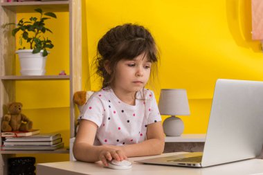 Online okul. Küçük kız dizüstü bilgisayar kullanıyor. Uzaktan eğitim ya da uzaktan öğrenme. Çocuk kız oturma odasında internetten ders çalışıyor. Covid-19 Coronavirüs.