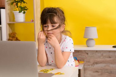 Online okul. Küçük kız dizüstü bilgisayar kullanıyor. Uzaktan eğitim ya da uzaktan öğrenme. Çocuk kız oturma odasında internetten ders çalışıyor. Covid-19 Coronavirüs.