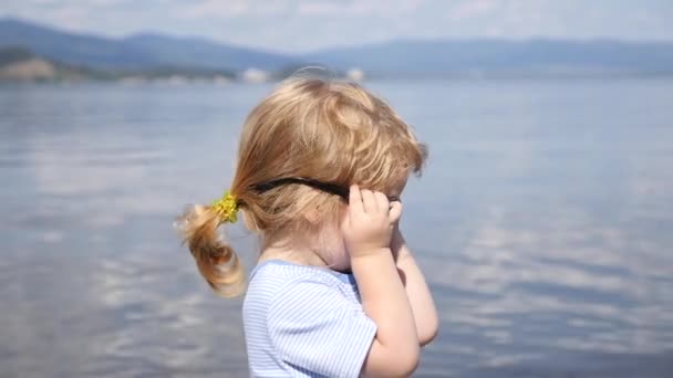 Мальчик в солнечных очках смотрит на озеро — стоковое видео