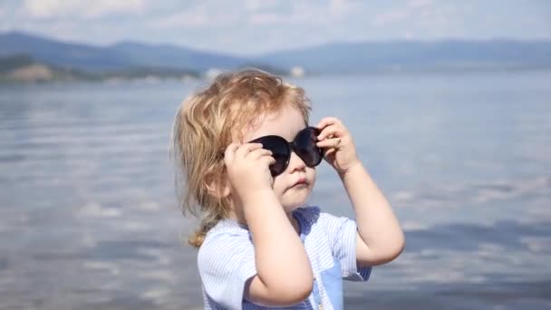 O rapaz de óculos de sol olha para o lago — Vídeo de Stock