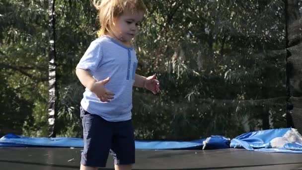 Gelukkig klein blond kind met bruine ogen springen eerst en plezier outdoor, slow-motion. Een klein trampoline op de achtertuin van het huis. Schattig kindje springen op een trampoline. — Stockvideo