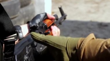 Titreyen elleri olan adam, vurulduktan sonra Kalaşnikof 'u tereddütle kontrol eder. Eğitmen, adama ne yapması gerektiğini gösterir. Yakın plan, Hd, ses yok.