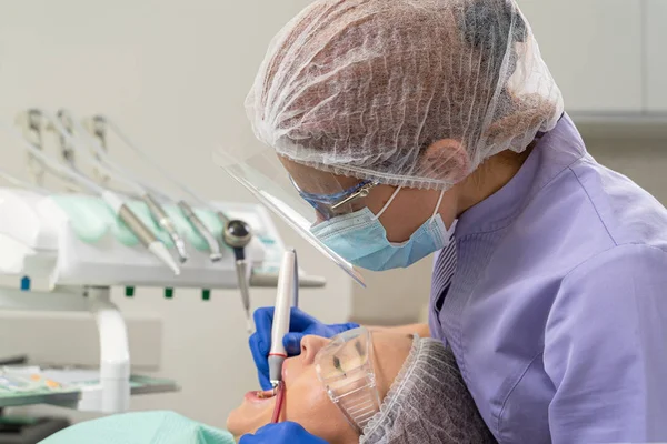 A dentist uses ultrasound and a saliva ejector to clean a patients dental calculus.