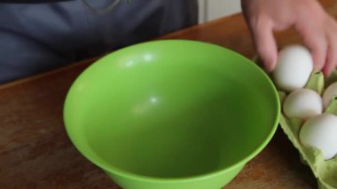 Karıştırıcıdan çırpıcılı bir adam tavuk yumurtasını kırıyor ve yeşil bir kaseye döküyor. Bir elin yakın çekimi, ses yok, Full Hd