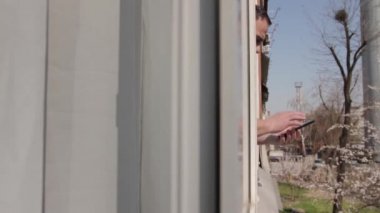 Bir adam açık bir pencerenin yanında akıllı bir telefonla kaydırıyor, aradığını buluyor, bir seçim yapıyor, neşeyle gülümsüyor. Pencere çerçevesinde, evden sokağa, soldan sağa hareket eden bir kamera var. Orta çekim, Full HD, ses yok.