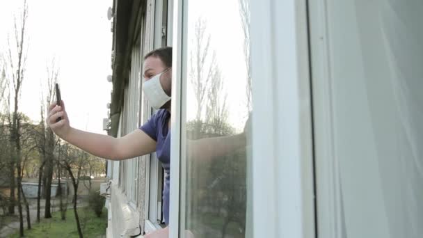 창문이 근처의 의료용 마스크를 남자가 스마트폰으로 비디오 채팅을 대화를 나누고 — 비디오